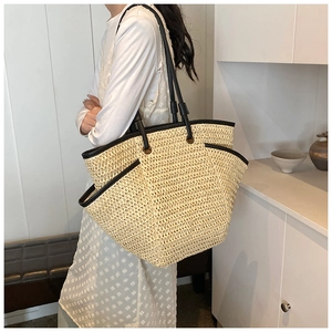 Detail of the woven straw tote bag featuring black leather straps and contrast trim
