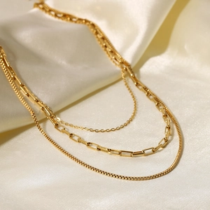 Three-layer 18K gold plated stainless steel layered necklace on cream silk fabric