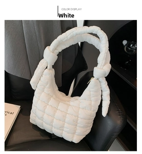 Detail of white quilted puffer bag with knotted shoulder strap and gold hardware accents