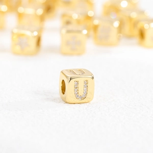 Macro shot of a 18k gold plated cube pendant featuring a sparkling zircon letter U