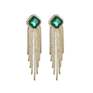 Detailed macro view of long tassel earrings with green square gemstones and silver rhinestones