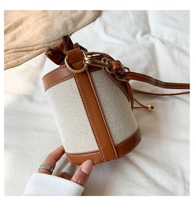 Close-up of woven canvas bucket bag with brown leather trim and golden drawstring beads