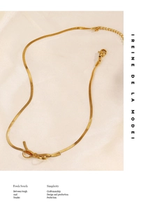 Macro shot of gold snake chain necklace featuring a bow pendant on beige silk fabric
