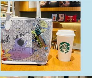 Close-up of green dinosaur truck keychain hanging on a white patterned tote bag