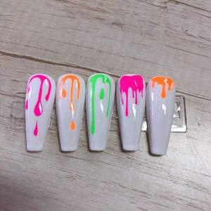 Close-up of neon drip paint patterns on white false nails with moon and star designs