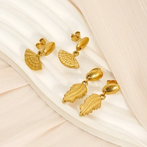 Détail de boucles d'oreilles éventail et plume dorées sur un tissu beige texturé