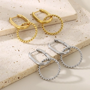 Minimalist twisted circle gold and silver stainless steel earrings on a beige stone surface