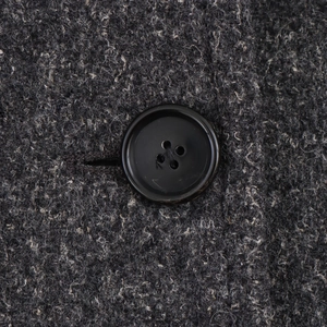 Close-up of black four-hole button on gray wool blend fabric texture of the coat