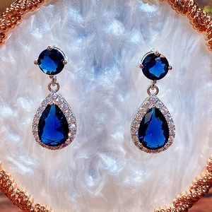 Detail shot of teardrop blue zircon earrings with a halo of small white crystals