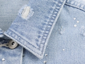 Détail du col d'une veste en jean bleu clair avec strass et texture denim vieillie