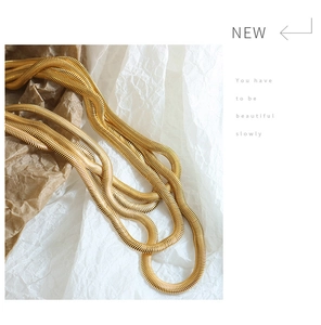 Detail van een meerlaagse gouden slangenketting met metaalglans op gestructureerd papier
