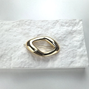 Minimalist gold metal hair clip with an irregular geometric oval design on textured stone