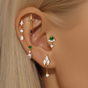 Detailed close-up of five gold-plated S925 silver ear studs with green and clear gems on ear