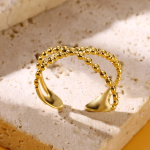 Detailed close-up of a golden double-cross ring with beaded texture on a stone surface