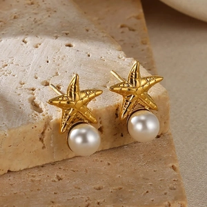 Golden starfish earrings with white pearls displayed on natural travertine stone
