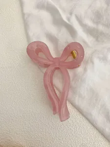 Detail of pink translucent bow hair claw clip with golden metal spring on white fabric