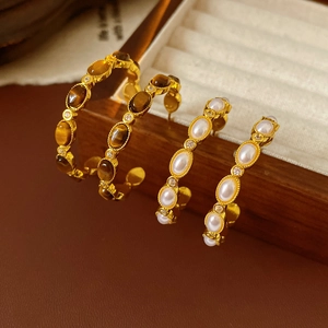 Dettaglio macro di orecchini vintage placcati oro con occhio di tigre e perle