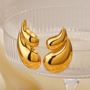 Polished 18K gold-plated teardrop stud earrings on a ribbed glass tray in high detail