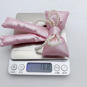 Detail shot of a pink satin bow keychain with pearls, weighing 16.8g on a digital scale