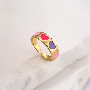 Detail view of gold heart ring with pink and purple enamel on white marble base