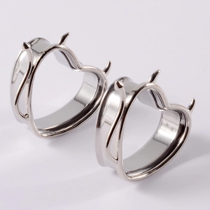 Detail view of silver heart-shaped ear gauges with devil horns in polished steel