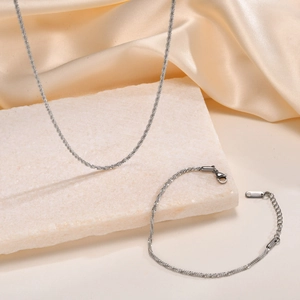 Elegant silver snowflake chain necklace and bracelet set on a white stone base