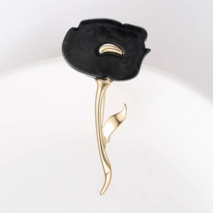 Close-up of elegant gold flower brooch with black resin petals on a white surface