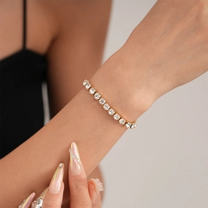 Detailed view of a gold tennis bracelet featuring square-cut cubic zirconia in prong setting