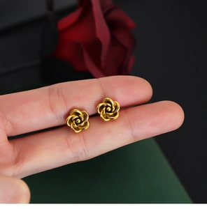Close-up of vintage gold rose stud earrings held by hand against red roses background