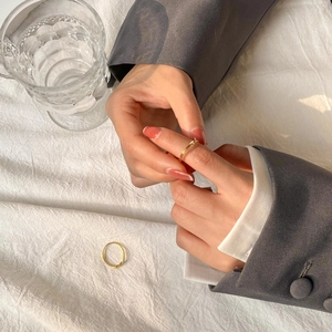 Close-up of minimalist gold twisted knot rings on a linen background with elegant sunlight