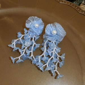 Détail de boucles d'oreilles fleurs en tulle bleu avec perles et longs pompons