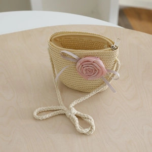 Detail of child's beige straw crossbody bag with pink fabric flower and ribbon accent
