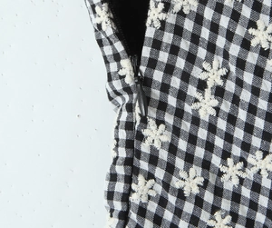 Detail of plaid fabric with white floral embroidery and invisible side zipper closure