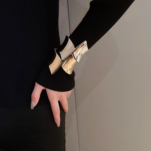Dettaglio di ampi bracciali metallici irregolari in oro e argento su una manica nera