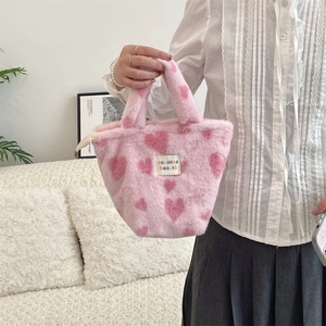 Detail of pink plush tote bag with heart patterns and woven label in cozy home setting