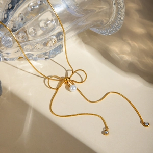 Close-up of 18k gold-plated bow necklace with pearl pendant and crystal accents on chain