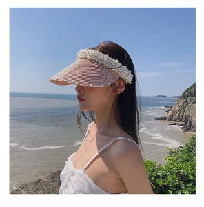 Detail of pink straw sun visor with pearl embellishments on brim for women