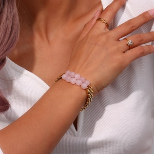 Close-up of golden stainless steel bracelet with pink stone inlay and matching rings