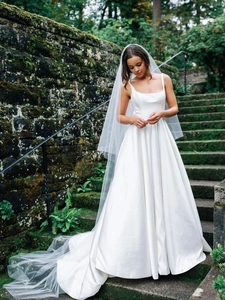 Detail of elegant white satin wedding dress with long tulle veil and minimalist square neck