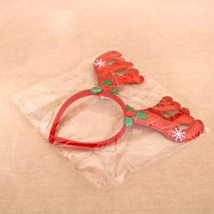 Close-up of red reindeer antler headband with snowflake and holly leaf in clear packaging