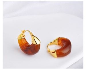 Detailed view of amber resin C-shaped earrings with golden metal clasps on white fabric