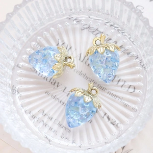 Macro shot of three transparent blue acrylic strawberry pendants with gold leaf detail