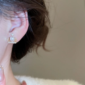 Close-up of elegant gold crown stud earring with pearls and zircons on ear