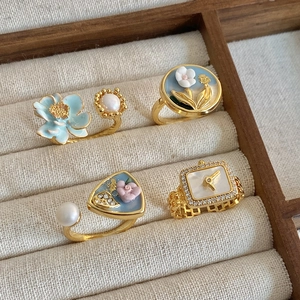 Baroque pearl and blue enamel flower gold rings set in a beige jewelry organizer tray