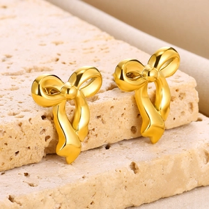 Macro shot of gold bow stud earrings with a satin matte finish on a beige stone base