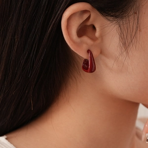 Gros plan de boucles d'oreilles en émail rouge foncé portées par un mannequin chic