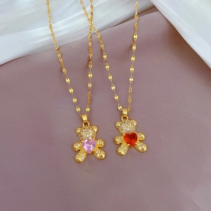Golden bear necklaces with pink and red heart zircons displayed on soft pink fabric