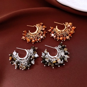 Detail of C-shaped beaded dangle earrings in gold and silver finish with textured stones