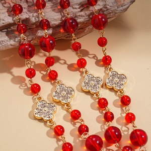 Detailed close-up of red crystal beads and gold diamond-set clover pendant on a stone