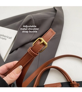 Detail of adjustable brown leather shoulder strap with gold buckle and lychee texture